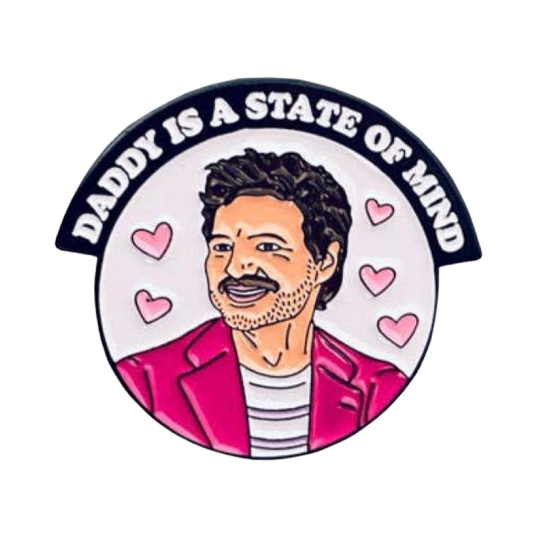 Light pink round enamel pin with an image of Pedro Pascal wearing a pink blazer and the phrase "Daddy Is A State of Mind"  in a black banner above the image of Pedro.