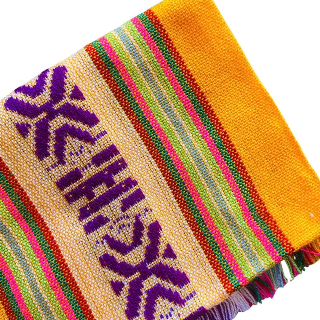 Close up of yellow Mexican Servilleta. Design features multicolored stripes with pattern.