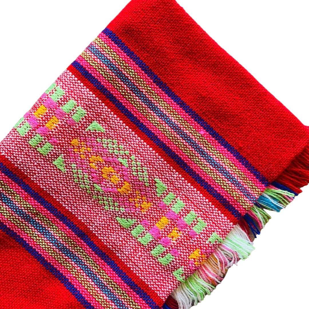 Close up of red Mexican Servilleta. Design features multicolored stripes with pattern. 