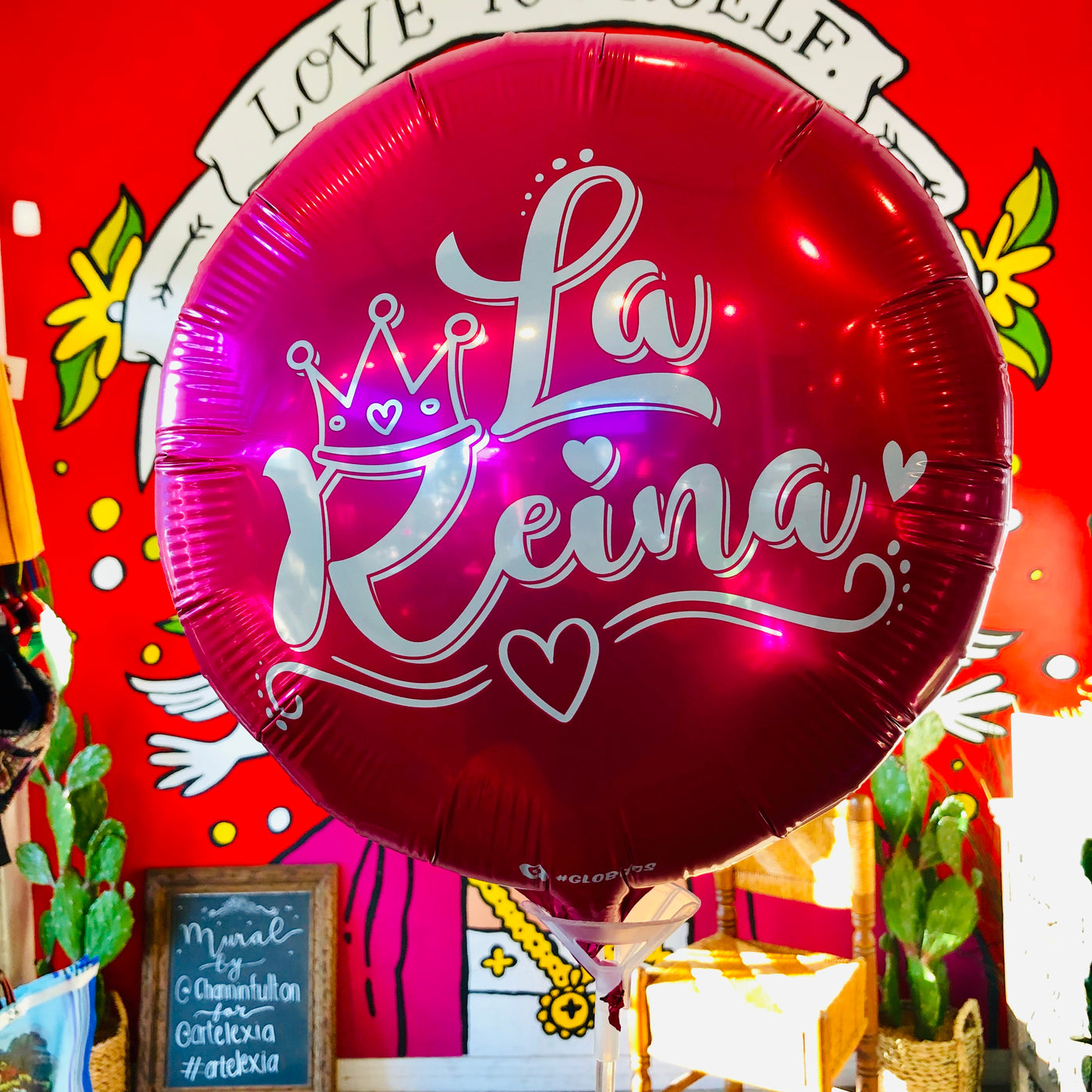 Hot pink mylar balloon with the words "La Reina" and a crown detailing on it.