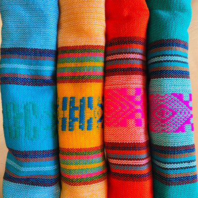 close up view of a set of four brightly colored napkins in the neon colors green, orange, yellow and blue with multi-colored designs.