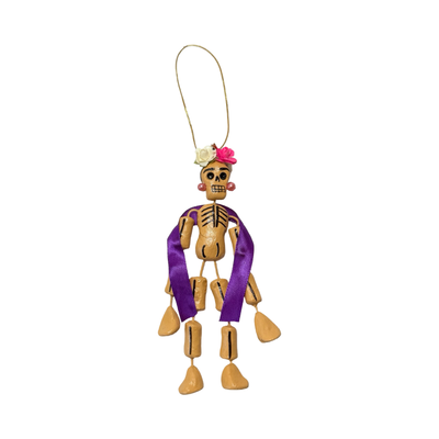 small Día de Muertos skeleton ornament with flowers, purple ribbon, and earrings.