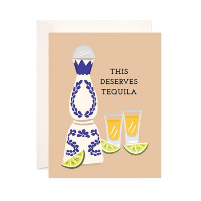 light brown card with a blue and white tequila bottle, 3 lime wedges and two shot glasses with the phrase This Deserves Tequila.