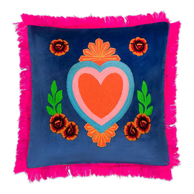 Square blue pillow with a central embroidered pink and orange heart, floral accents, and bright pink fringe trim.