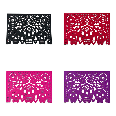 4 mutlicolored felt papel picado inspired placemats that features a trio of skulls design with flowers and bone crosses.