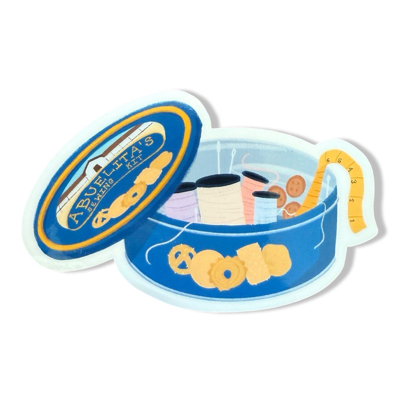 Sticker of an open blue cookie tin labeled “Abuelita’s Sewing Kit,” filled with spools of thread, buttons, a measuring tape, and a few cookies
