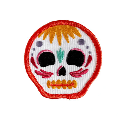 Embroidered iron-on patch shaped like a colorful calavera skull with orange, pink, and teal details outlined in red.