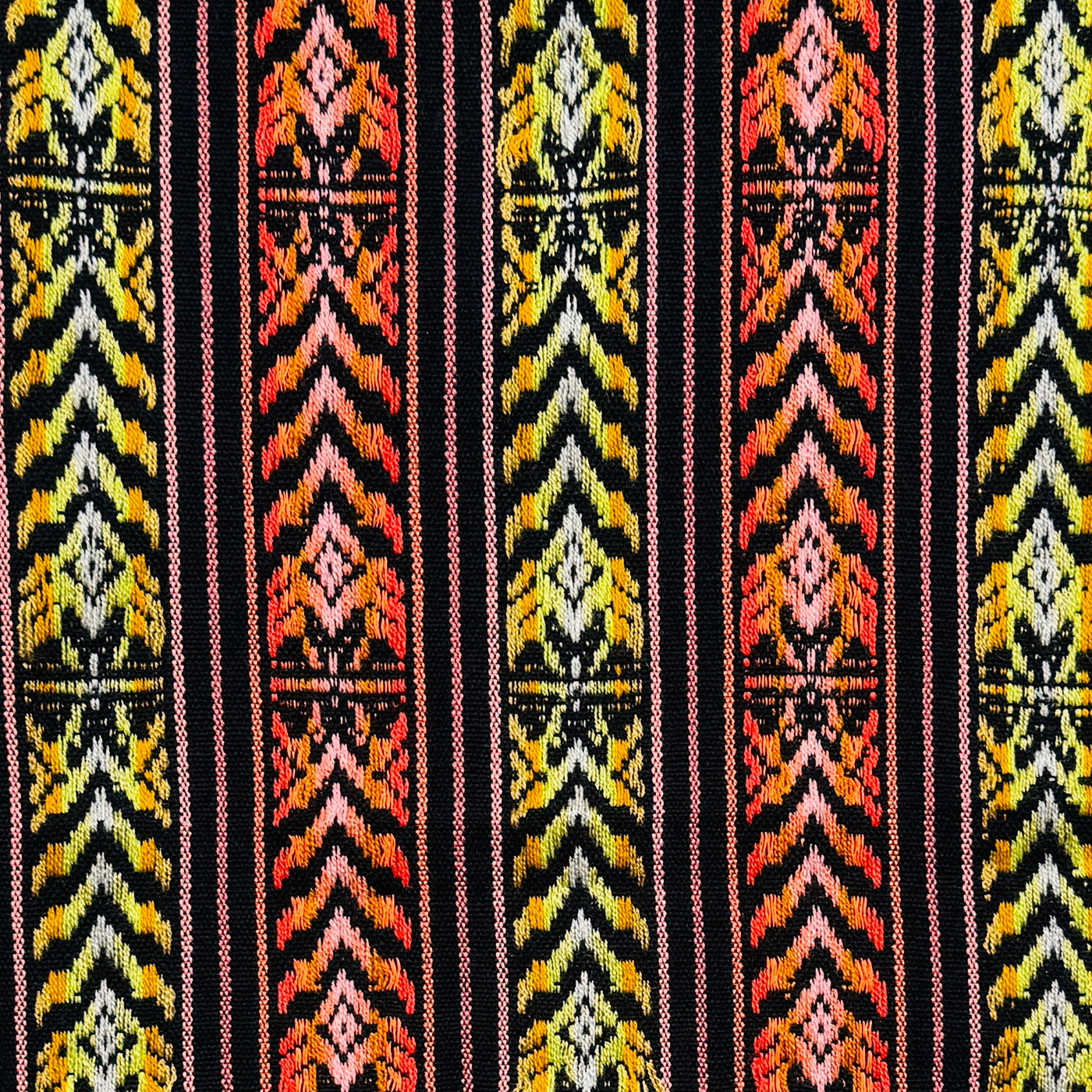 close up view of a Colorful woven Cambaya table runner from Mexico, featuring intricate geometric patterns in yellow, orange, and black with multicolored fringed ends.