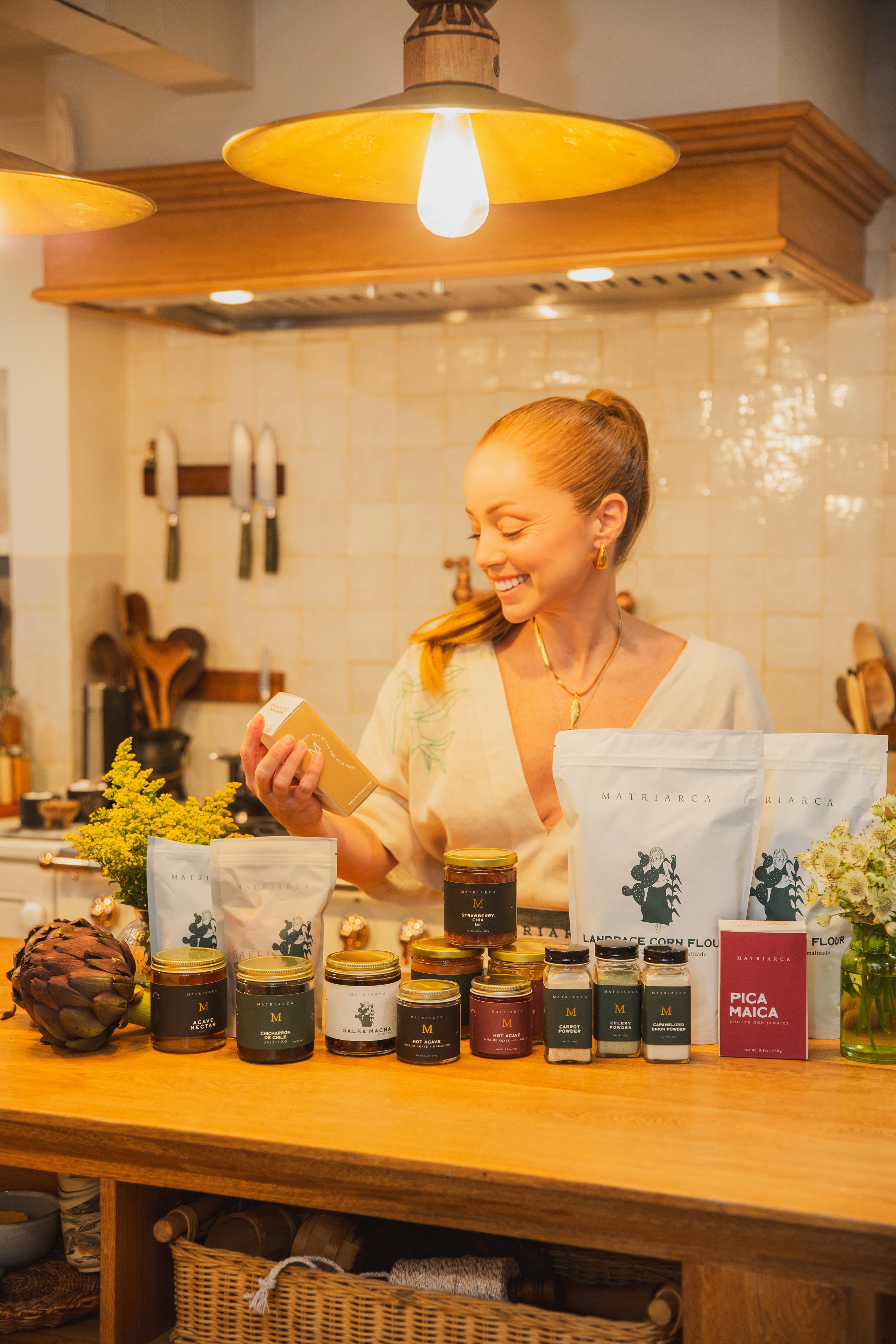 Chef Marcela Valladolid in a kitchen with various jars and bags of Matriarca food products