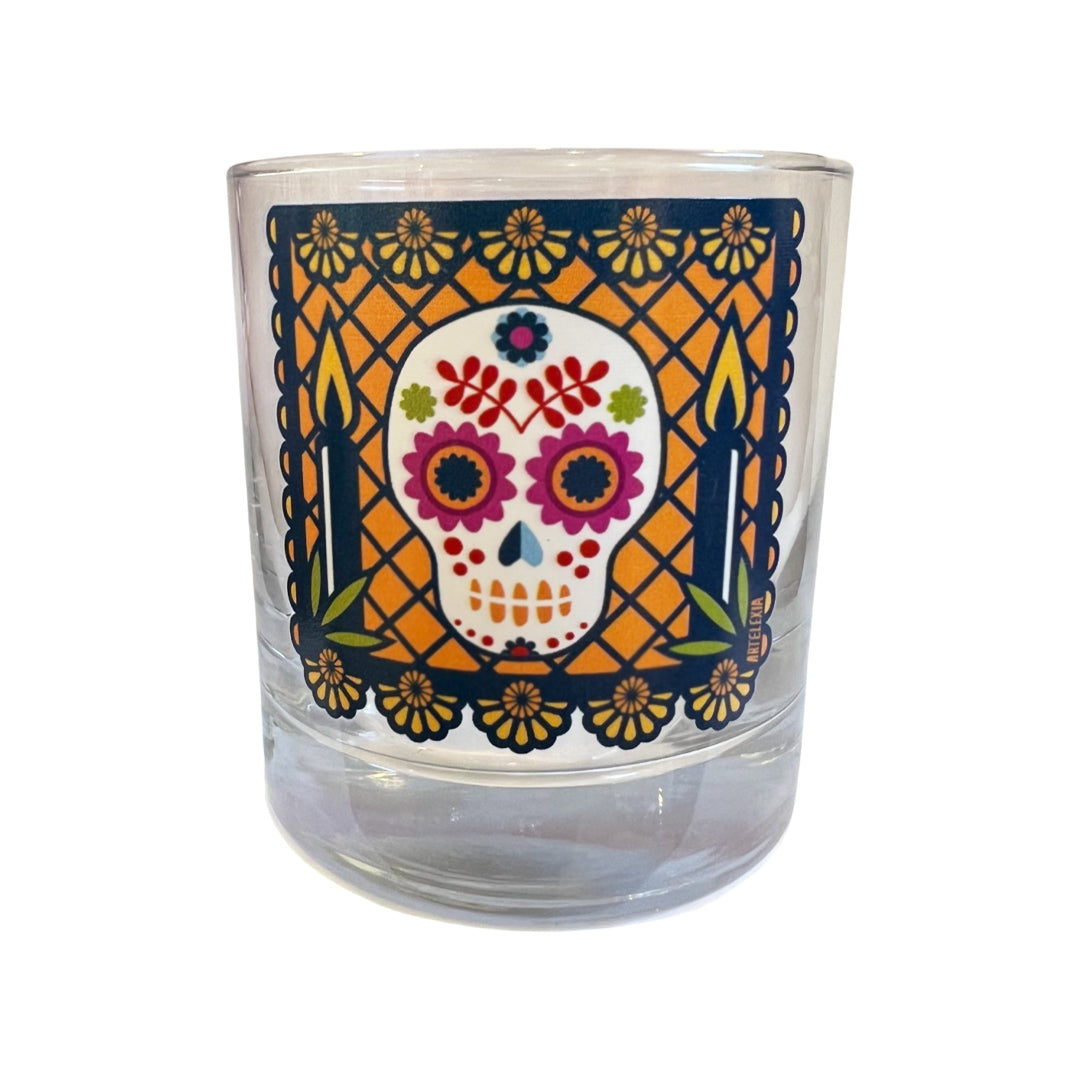 Photo of side view of cocktail glass featuring a navy blue colored papel picado with a sugar skull in the center & an orange background