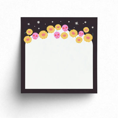 Sticky note pad with a black border decorated with yellow marigolds, pink calaveras, and white stars across the top.