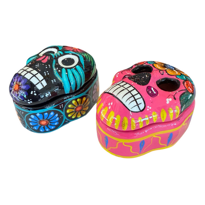 Side view of a set of colorful skull trinket boxes. One being pink with a colorful floral design and the other being Black with a colorful design.