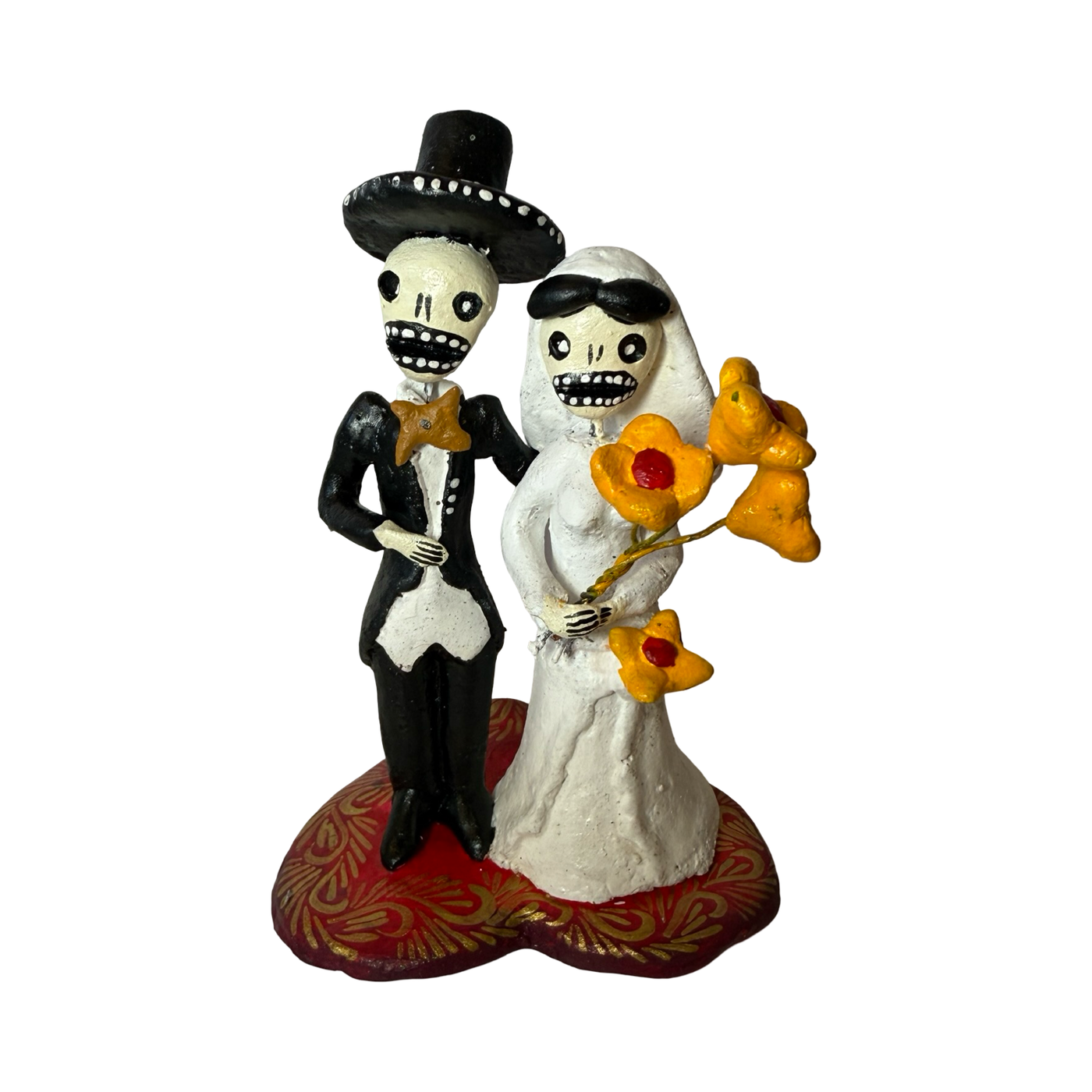 Handmade Día de Muertos figurine of a skeletal bride and groom standing together, the bride holding yellow flowers, both on a decorative red base shaped like a heart.