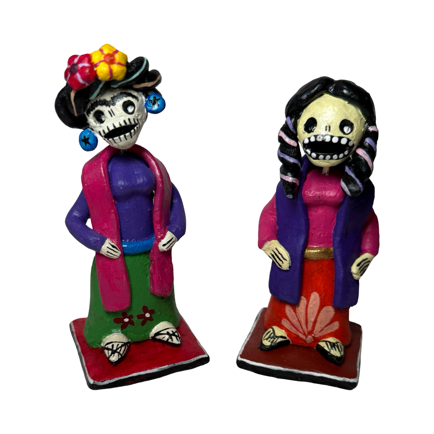 Two colorful hand-painted Día de Muertos skeleton figurines in traditional clothing, one with a flowered crown and the other with braided hair, both standing on square bases.