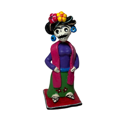 Colorful hand-painted Día de Muertos Frida Kahlo skeleton figurine in traditional clothing and a flower crown standing on square base.