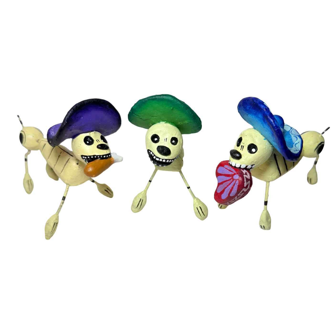 Three handcrafted Día de Muertos skeleton dog figurines wearing colorful sombreros. One carries a piece of pan dulce, another holds a butterfly-shaped heart, and the third features a bright grin, all painted in vibrant detail.