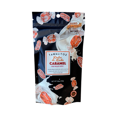 Black stand-up pouch of Tamalitoz “Dulce de Leche Caramel – The Milky Güey,” featuring milk-splash graphics, pecan and wrapped-caramel illustrations, and a label noting real milk, pecans, and sea salt; 3.5 oz