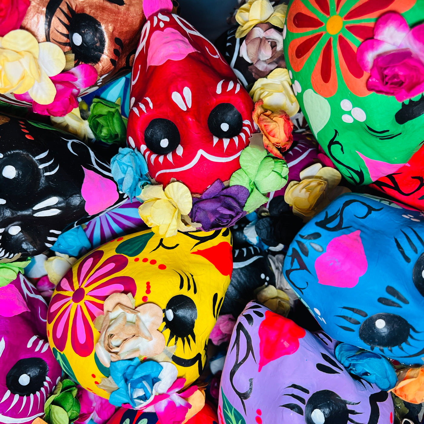 close up photo of a pile of view of colorful paper mache frida sugar skulls in multiple colors featuring a flower crown on each.