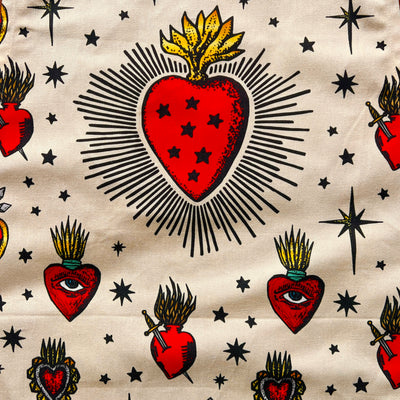 close of view of a cream apron with various images of sacred hearts with eyes, stars and daggers in the center of them