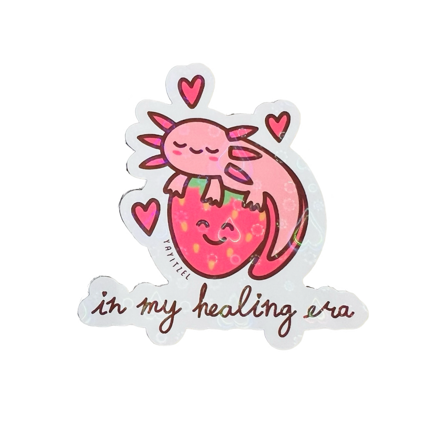 A holographic sticker featuring a cute pink axolotl resting on a smiling strawberry. The design includes small hearts floating around the axolotl. Below the illustration, the phrase "in my healing era" is written in a playful, cursive font.