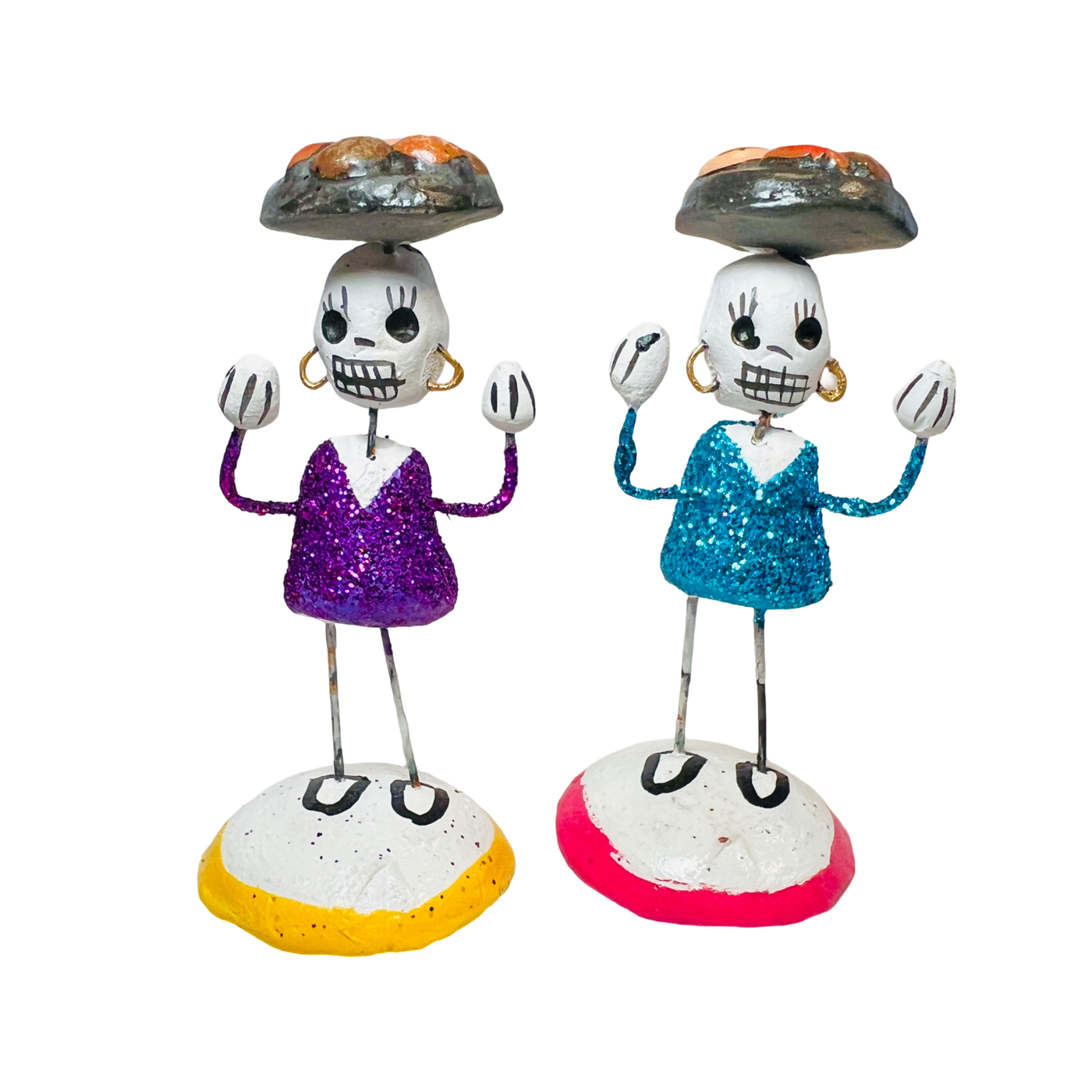 A pair of painted clay skeletons with a tray of bread on their head.