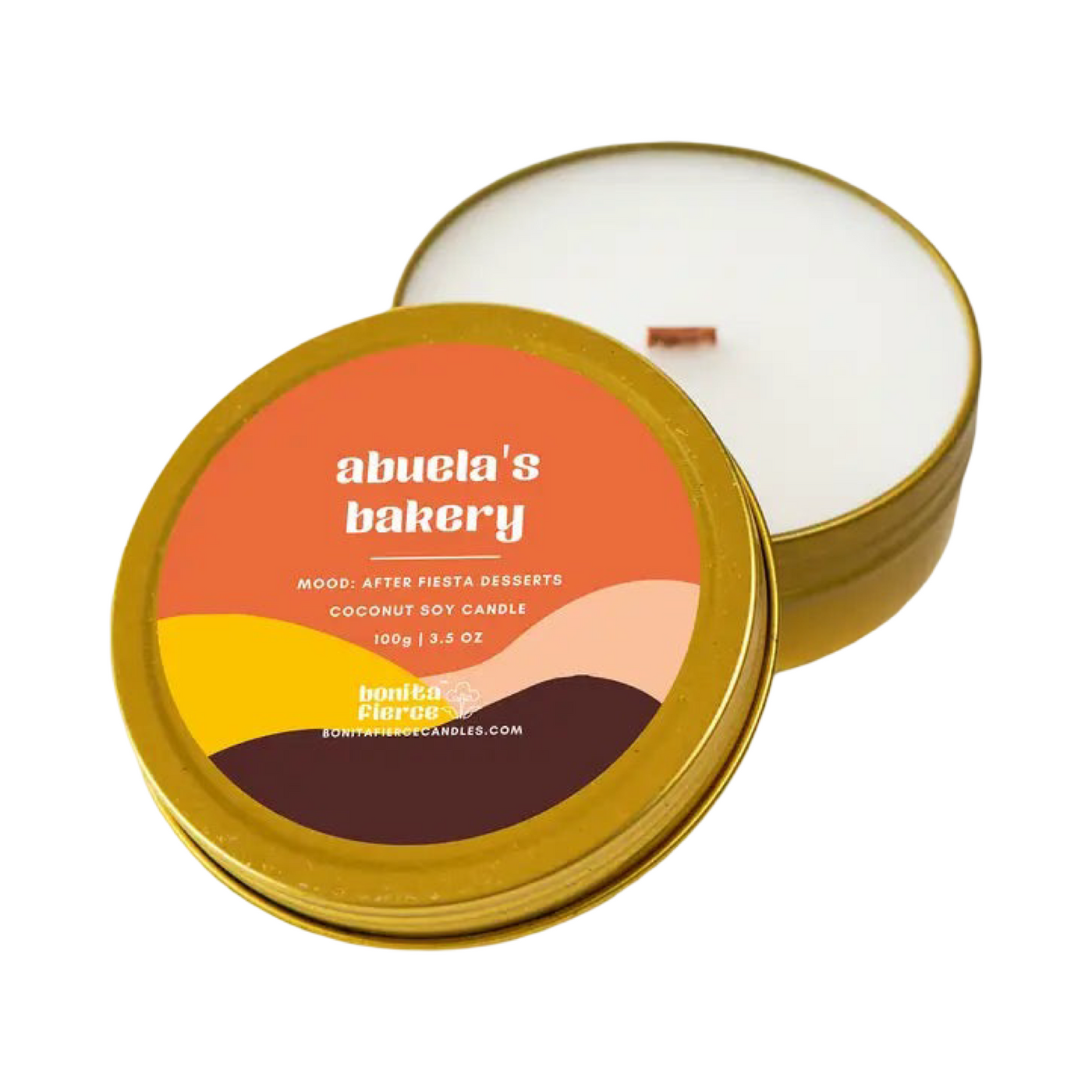 3.5 oz white candle in a gold tin jar with a wooden wick and a multi-colored banded label with the name Abuela's Bakery.