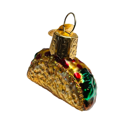 Angled view of a Mini glass taco ornament with detailed textures and glitter accents, featuring lettuce, tomato, and cheese toppings