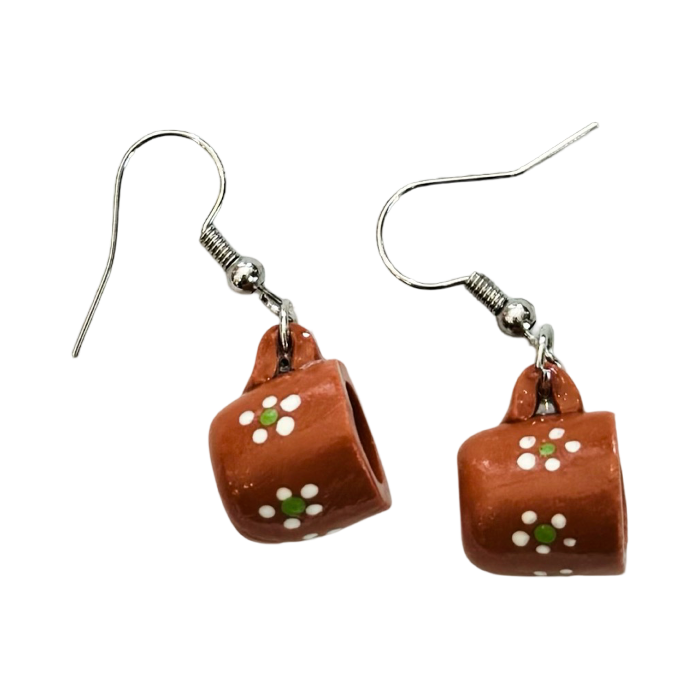 A pair of earrings shaped like traditional Mexican Barro mugs, made from terracotta clay with hand-painted white and green floral designs, attached to silver hooks.