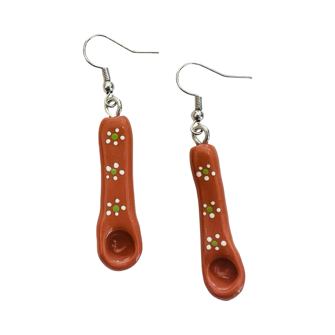 A pair of earrings shaped like traditional Mexican Barro spoons, made from terracotta clay with hand-painted white and green floral designs, attached to silver hooks.