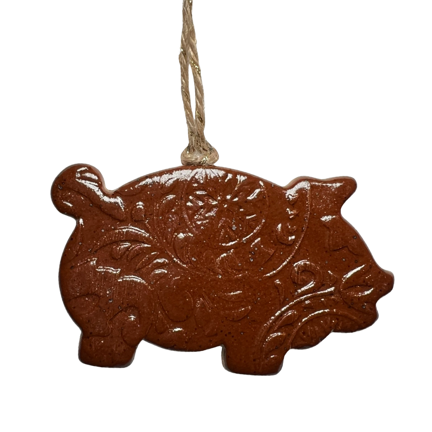 A handmade ceramic ornament shaped like a traditional Mexican Marranito pastry, featuring intricate embossed patterns and a glossy finish, hanging from a natural twine string.