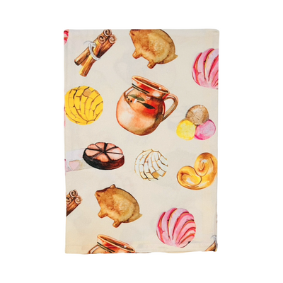 A beige kitchen towel folded in quarters with colorful illustrations of Mexican sweet bread, such as conchas, marranitos, polvorones, and cuernitos, alongside cinnamon sticks and a traditional clay mug.