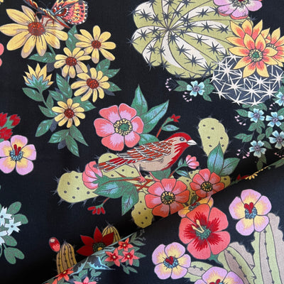 Close up of Black fabric with images of various types of green cactus with multi-colored  flowers and birds.