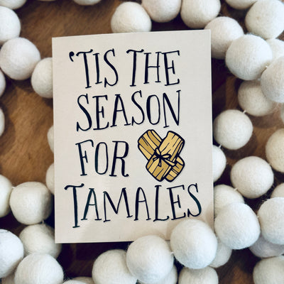 Photo of greeting card with beige background & black text that reads "'Tis The Season For Tamales"