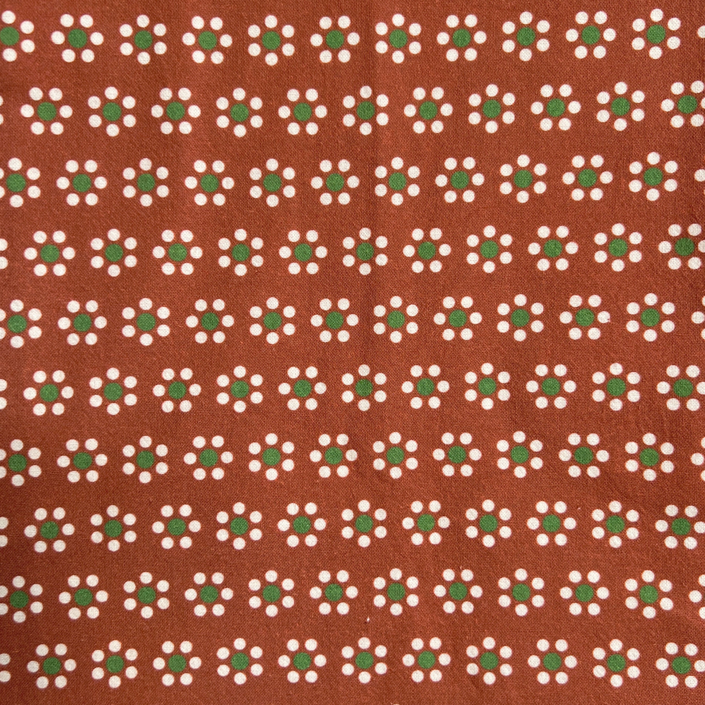 close up view of a terracotta-colored kitchen towel featuring a repeating floral pattern inspired by traditional Mexican barro pottery. The design includes small white and green flowers