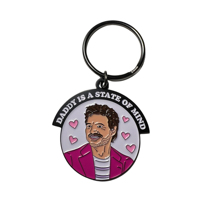 Enamel keychain of Pedro Pascal wearing a pink blazer surrounded by pink hearts. Features the phrase Daddy Is A State of Mind