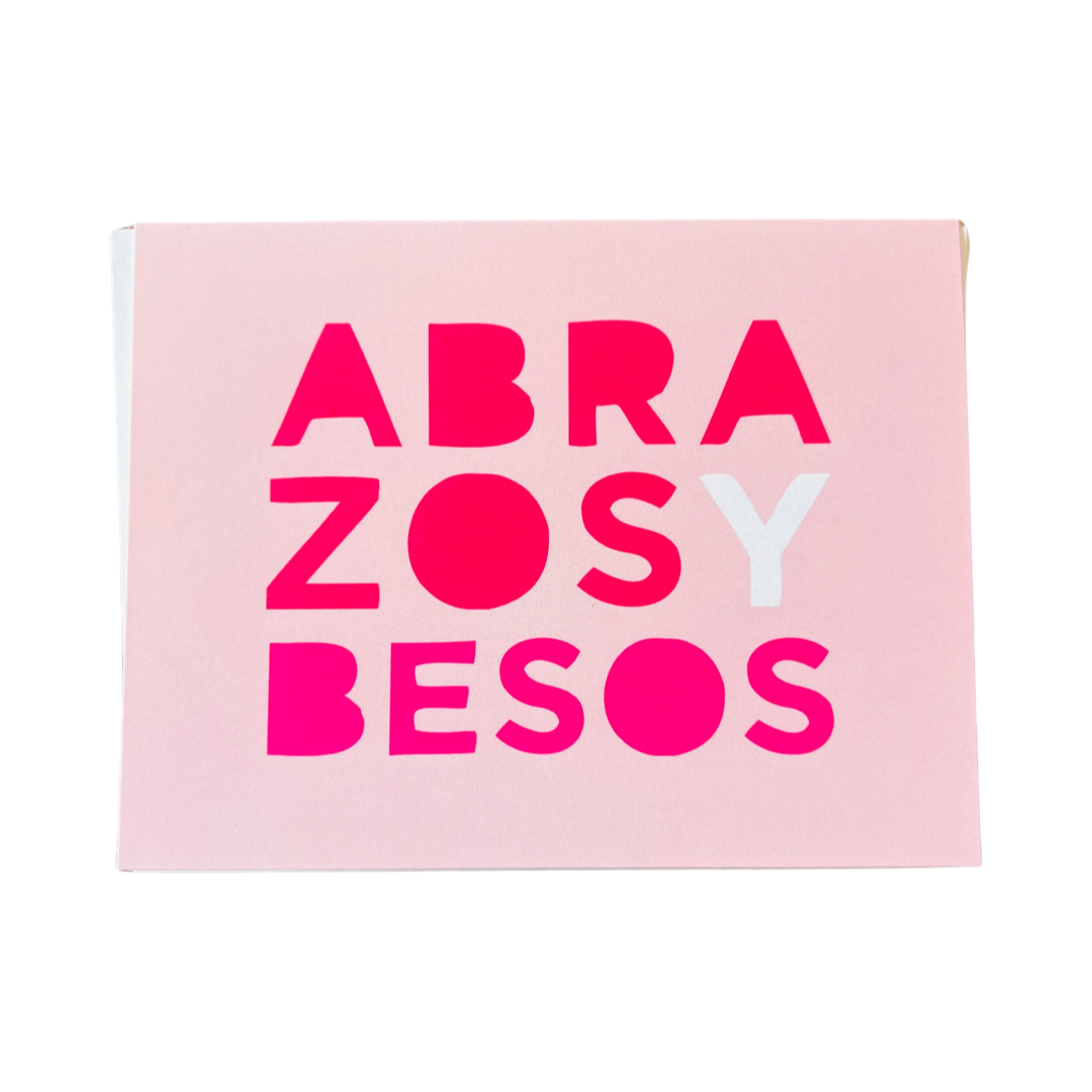 pink card with the phrase Abrazos y Besos in pink, and white lettering.