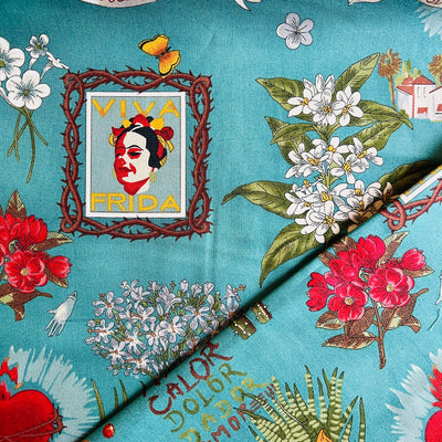 Fabric with the images various flowers, cacti, sacred heart and a framed image of Frida with a teal background