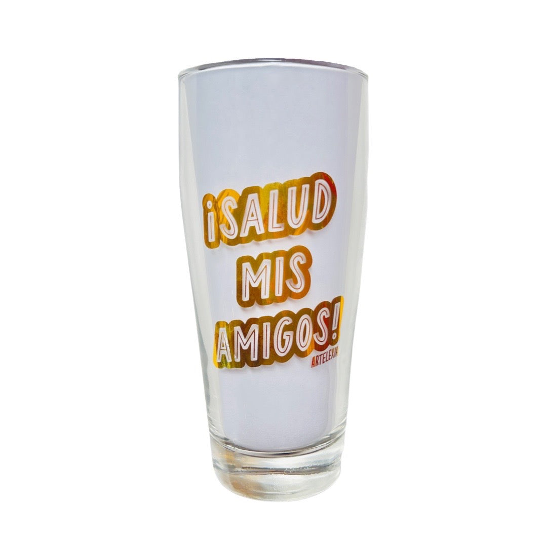 Clear glass tumbler with the phrase Salud Mis Amigos in gold lettering.