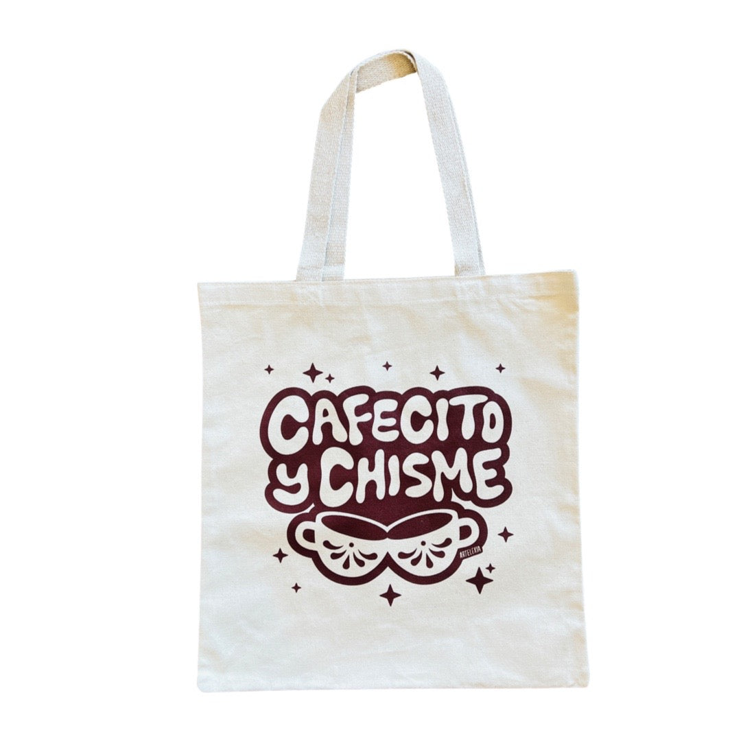 Natural canvas tote bag with the phrase Cafecito y Chisme in brown lettering and a set of two mugs underneath the phrase.