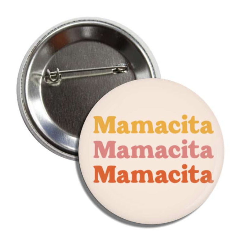 Set of pin-back buttons with one showing the back of it and the other one is cream with the phrase Mamacita, 3 times, in yellow, pink and orange lettering.