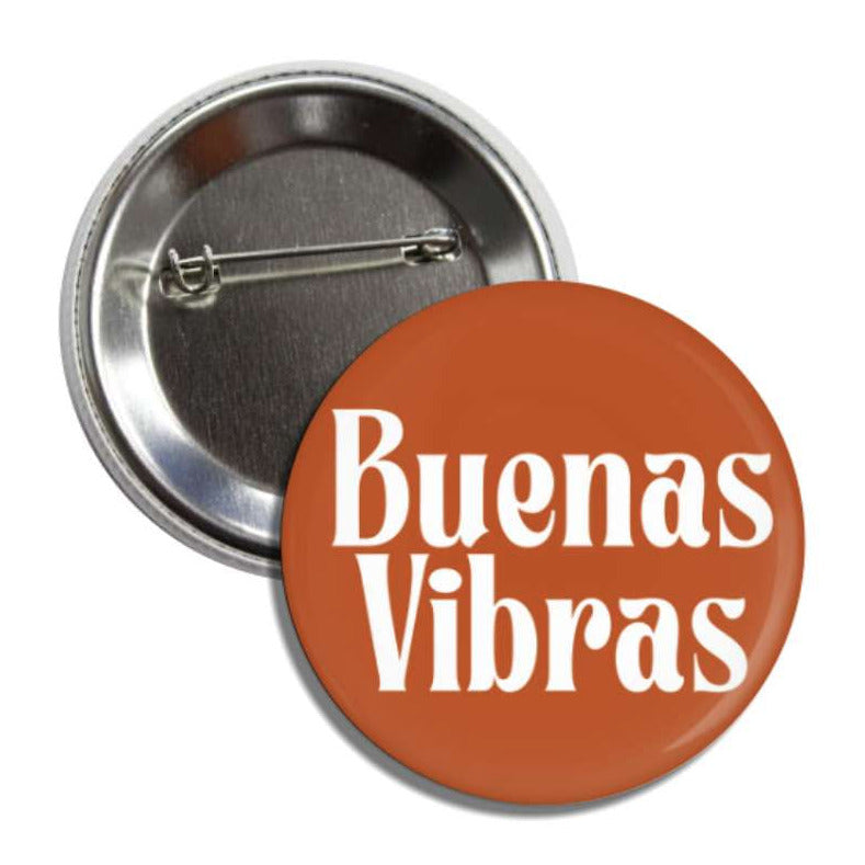 Set of pin-back buttons with one showing the back of it and the other one is sienna with the phrase Buenas Vibras in white lettering.