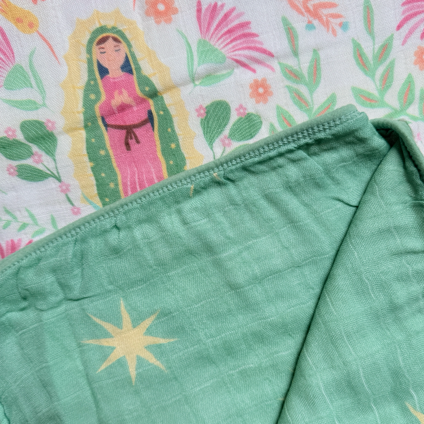 Cream quilt with images of Our Lady of Guadalupe with a pink, green and yellow floral design on one side and a green background with gold stars on the other side.
