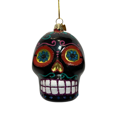 A vibrant black glass ornament in the shape of a Día de los Muertos sugar skull, featuring intricate glitter designs, colorful floral eye accents, and a cheerful, toothy grin.