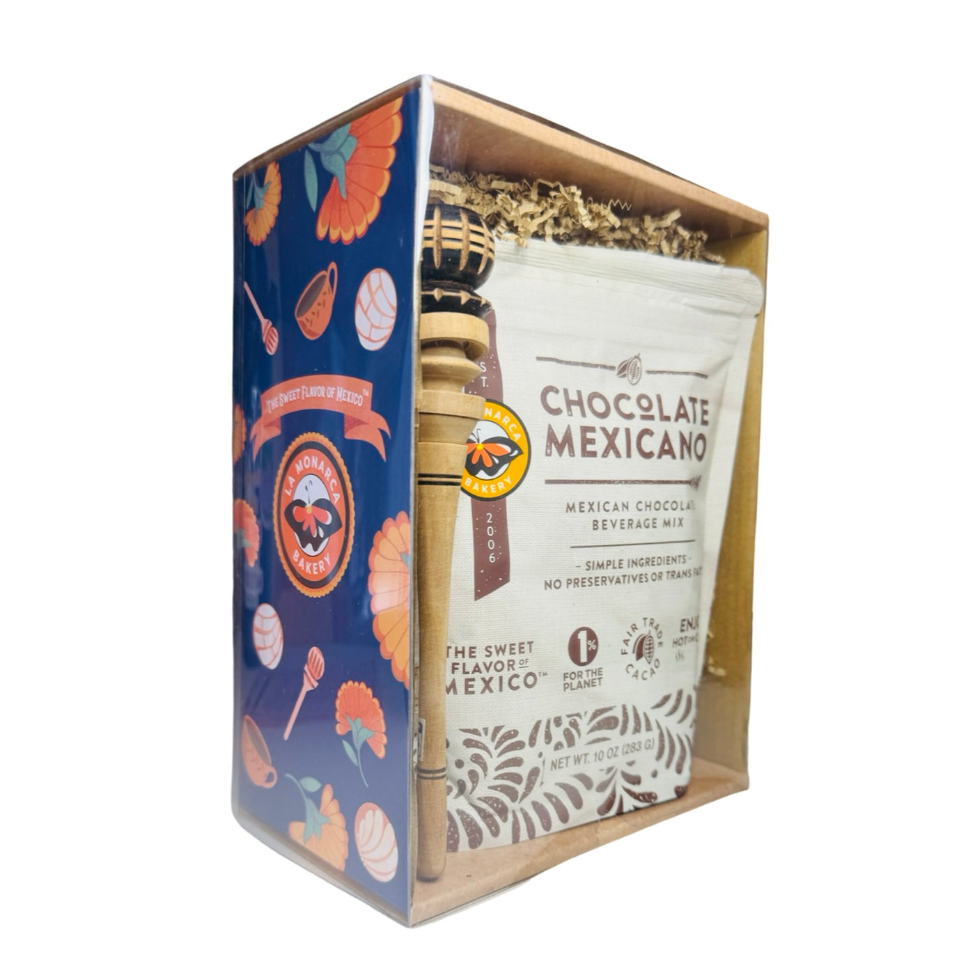 Gift box with La Monarca Bakery “Chocolate Mexicano” beverage mix and a small wooden molinillo whisk, visible through a clear window with blue floral side panel.