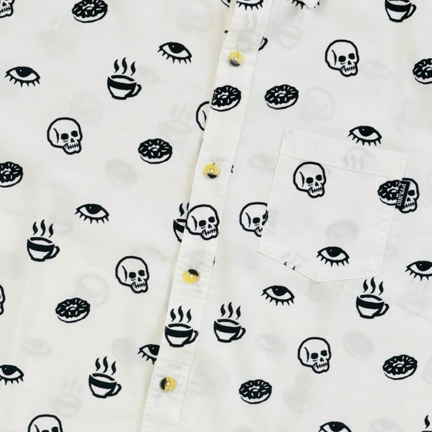 Close up view of a white short-sleeve button-down shirt with allover black prints of coffee cups, donuts, skulls, and eyes.