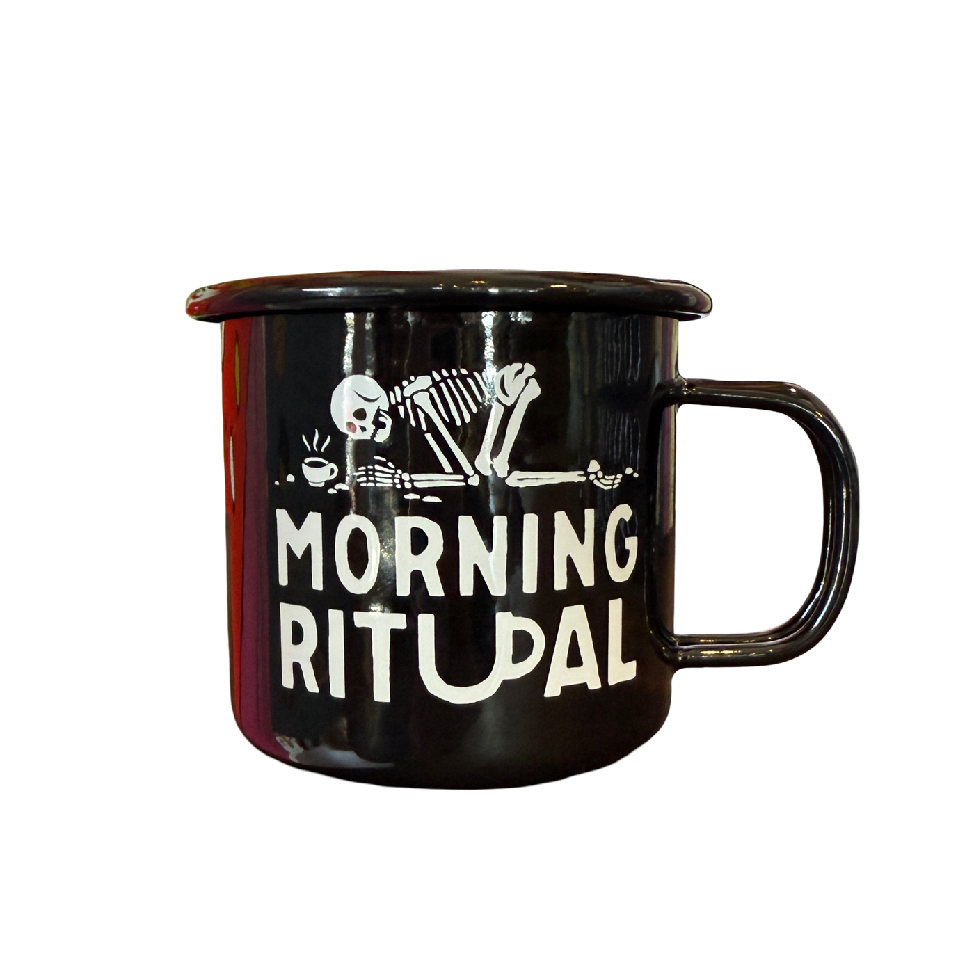 Black enamel mug with a white illustration of a skeleton slumped in front of a steaming coffee cup and the words “MORNING RITUAL” printed underneath.