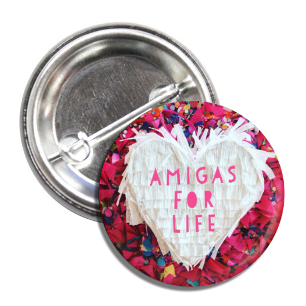 Round pin back button with a confetti back ground and features a white pinata heart with the phrase Amigas for Life.