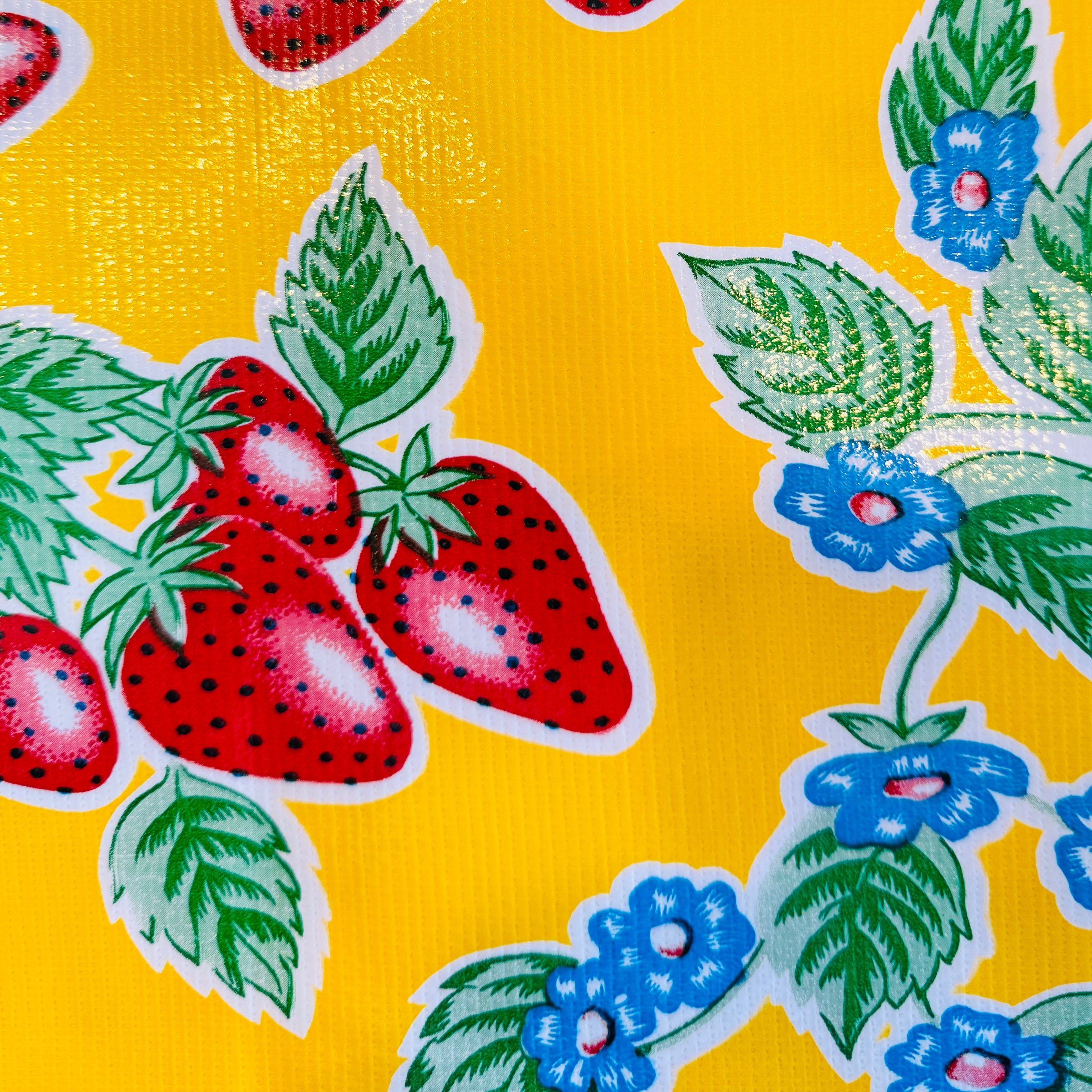 yellow oilcloth table cover featuring  an illustrated strawberry pattern with blue flowers.