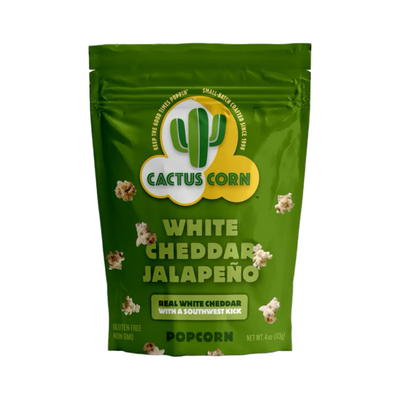 A 4oz green bag of Cactus Corn White Cheddar Jalapeño Popcorn featuring popped kernels scattered across the packaging. The bag displays the brand logo with a cactus and text that reads “White Cheddar Jalapeño Popcorn.”