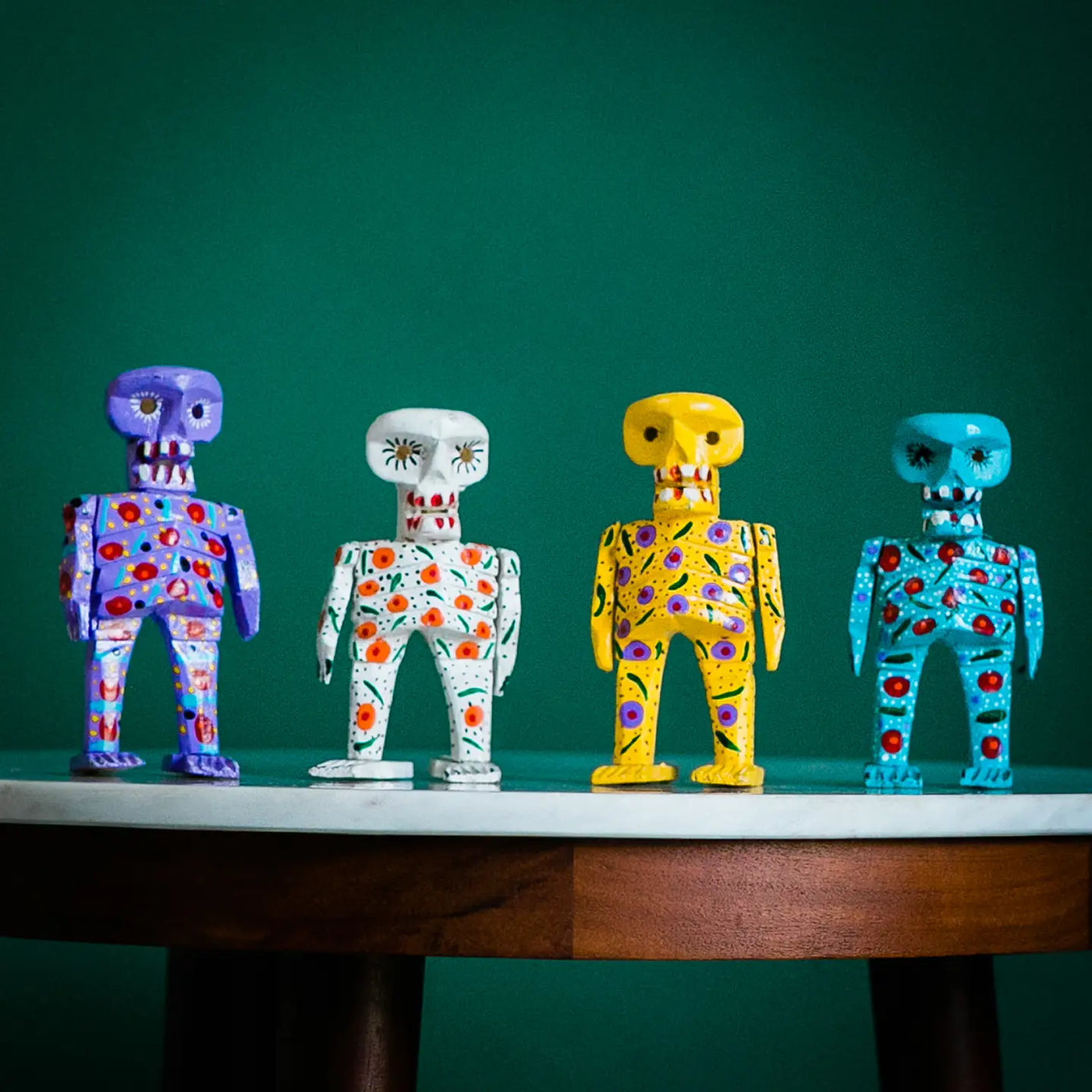 Colorful hand-painted wooden sugar skull skeleton figures in purple, white, yellow, and blue with decorative patterns.
